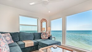 A modern living room with a large window overlooking the ocean, a dark blue sofa, a glass coffee table, and a wooden side table. - Windows on the Water "W.O.W"  An ocean front oasis!   (Captiva)