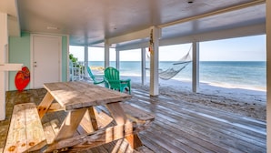 A beachside patio with a wooden table and chairs, a hammock, and a view of the ocean. - Windows on the Water "W.O.W"  An ocean front oasis!   (Captiva)