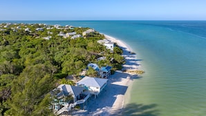 An aerial view of a coastal property with beachfront houses, a sandy beach, and a clear blue ocean. - Windows on the Water "W.O.W"  An ocean front oasis!   (Captiva)