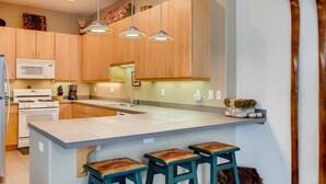 Una cucina moderna con mobili in legno, un'isola centrale con sgabelli, illuminazione a sospensione e un forno a microonde.
