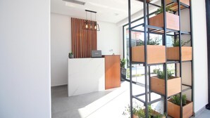 Una moderna zona de recepción con un mostrador blanco, una jardinera de madera vertical con plantas, y una lámpara colgante.