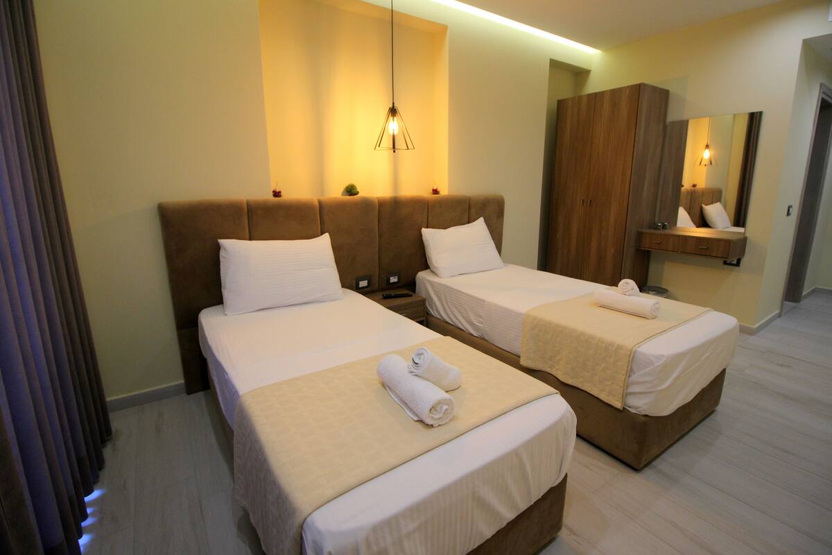 Habitación de hotel con dos camas, un armario de madera, un espejo y una lámpara colgante.
