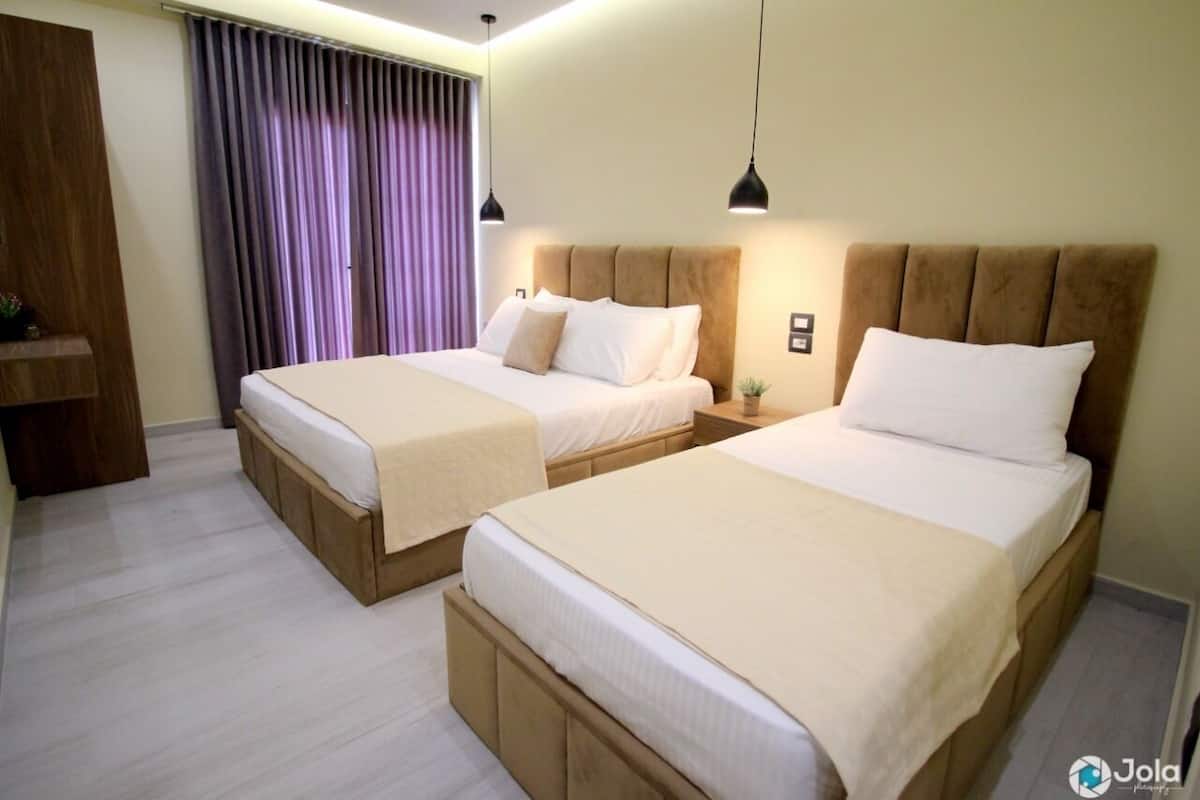 Una habitación de hotel con dos camas, un armario de madera y una ventana con cortinas moradas.