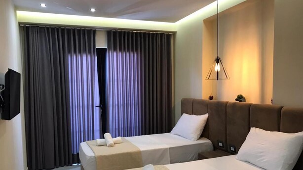 Una habitación de hotel con dos camas, un televisor montado en la pared y un amplio ventanal con cortinas.
