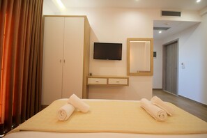 Une chambre d’hôtel avec un lit, deux serviettes enroulées, une télévision, un miroir et une armoire.
