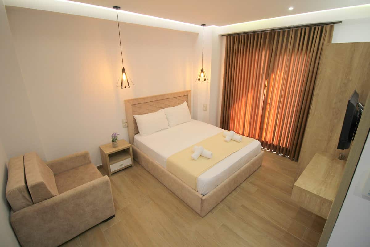 Una habitación de hotel moderna con una cama grande, un sofá, una mesita de noche y un televisor.