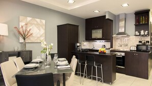 Una cocina moderna con armarios oscuros, una isla central y un comedor con mesa y sillas de vidrio.