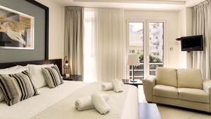 Habitación de hotel con una cama grande, un sofá, un televisor y una ventana con cortinas.