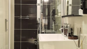 Un baño moderno con ducha acristalada, lavabo blanco y encimera oscura.
