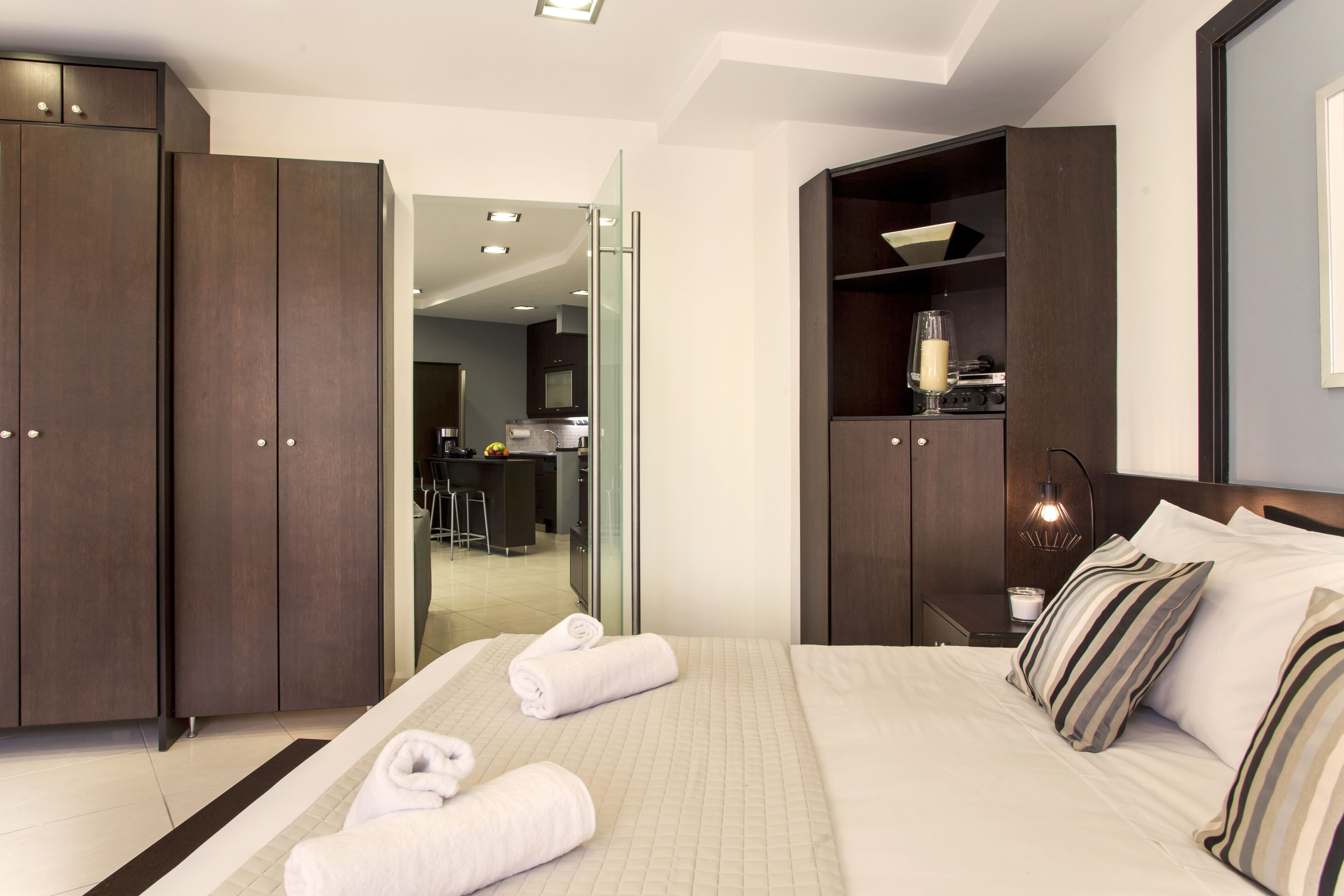 A modern hotel room with a large bed, a desk, and a kitchenette.