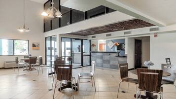 A spacious indoor area with multiple seating arrangements, including round tables and chairs, and a reception desk.