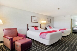 A hotel room with two beds, a chair, a lamp, and a framed picture on the wall.