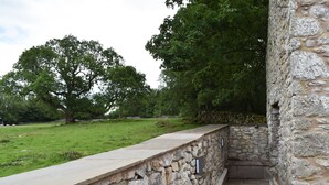 A stone pathway leading to a stone wall with a grassy field and trees in the background.
