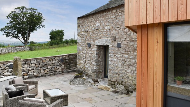 A stone building with a wooden exterior, a stone wall, and a large tree in the background.