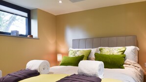 A hotel room with a bed, green and white pillows, a headboard, and a window with blinds.