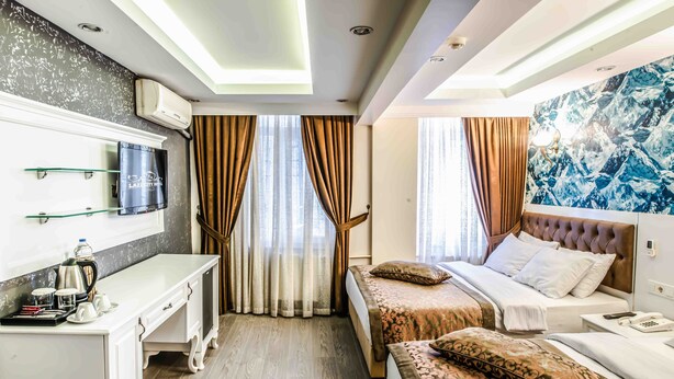 A hotel room with a desk, two beds, a mounted TV, and a large window with curtains. - Lazz City Hotel (Istanbul)