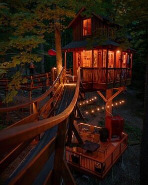Una cabaña de madera con una terraza de varios niveles, un tobogán y luces colgantes.