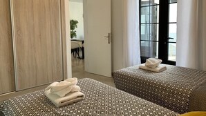 A hotel room with two beds, a wardrobe, a bathroom, and a view through a glass door. - 5 Star,  2 x True  Ensuite’s, Beach 20 meters,  Pool,  AC, FREE WIFI, Full TV.  (Puerto del Carmen)