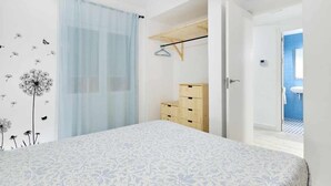 Een slaapkamer met een bed, een houten dressoir, een kledingrek en een badkamer die door een open deur zichtbaar is.