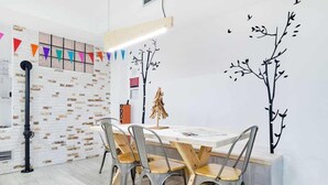 Een eetgedeelte met een witte tafel, vier stoelen en een decoratieve muurschildering van een boom.
