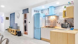 Een compacte keuken met een blauwe koelkast, een spoelbak en een fornuis. Er is een houten kastje en een decoratieve spatwand.