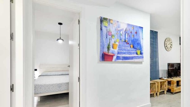 Een slaapkamer met een bed, een schilderij van kleurrijke treden, een klok en een tv-meubel.