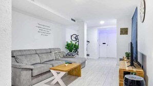 Een moderne woonkamer met een grijze bank, een houten salontafel en een tv op een houten dressoir.