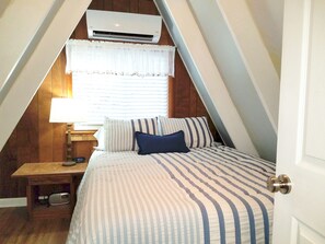 A bedroom with a bed, a nightstand, a lamp, and an air conditioning unit.