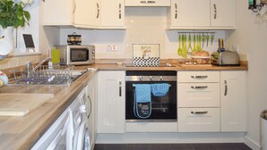 Eine moderne Küche mit weißen Schränken, einem Geschirrspüler, einem Backofen, einer Mikrowelle und einem Toaster. Ein kleines Fenster mit Vorhängen, eine Spüle und ein Geschirrgestell sind ebenfalls vorhanden.