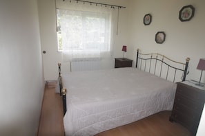 A bedroom with a bed, a nightstand, a dresser, and a window with curtains.