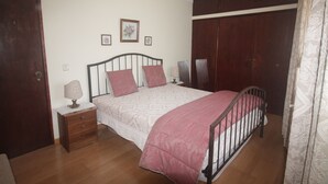 Une chambre à coucher comprenant un lit, une armoire en bois, une table de chevet et une petite table de nuit.