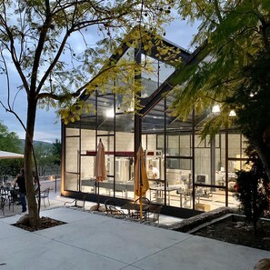 Ein modernes Glasgebäude mit Terrasse, Sitzgelegenheiten im Freien und sichtbarer Küchenausstattung.