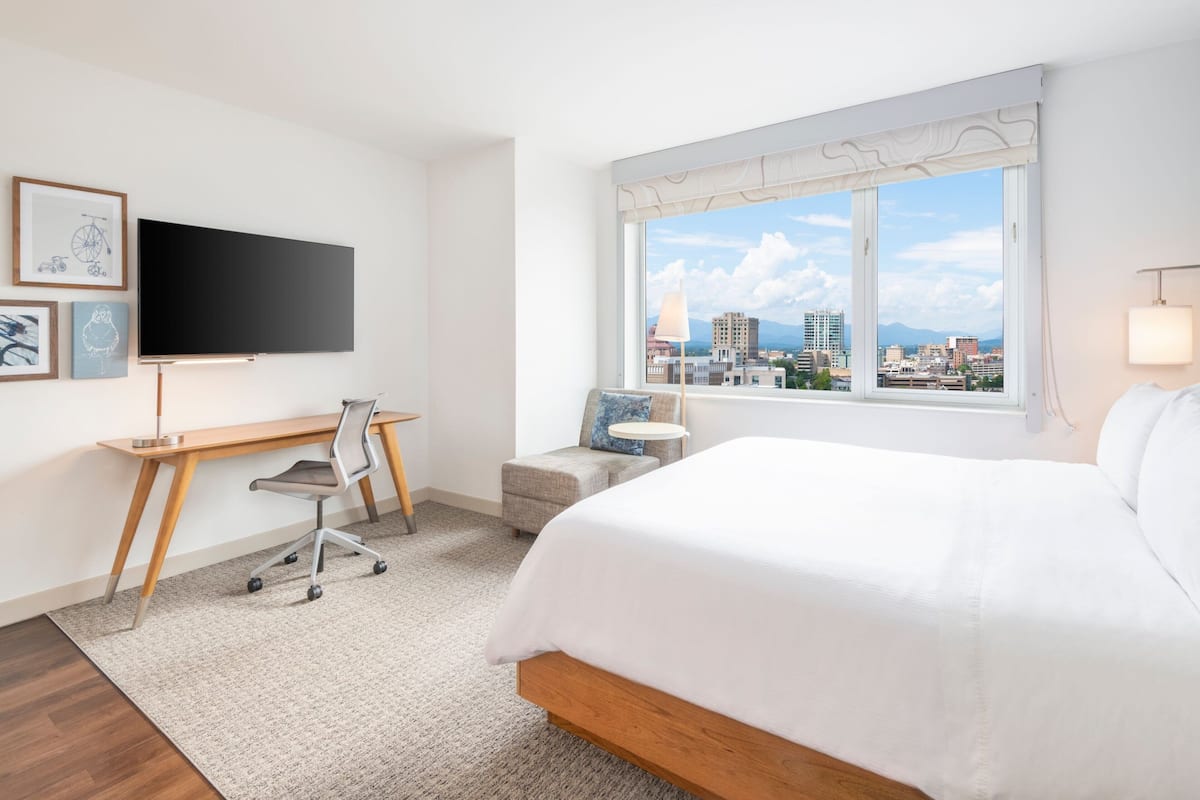 Een hotelkamer met een bed, bureau, stoel, televisie en raam met uitzicht op de stad.