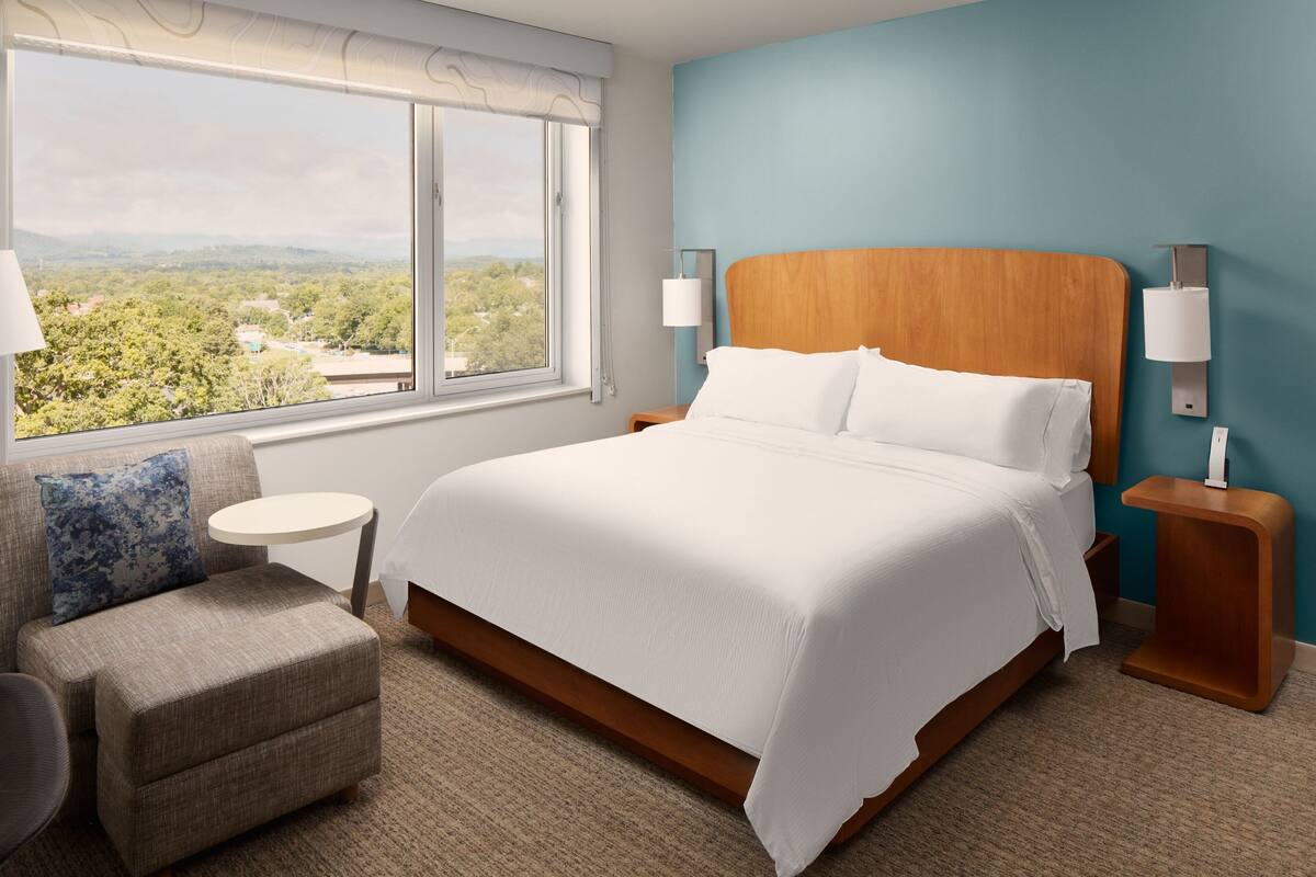 Een hotelkamer met een groot bed, uitzicht op de omgeving, een klein rond tafeltje en een stoel.
