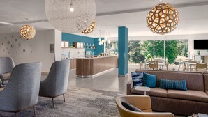 Eine moderne Hotelhalle mit einer zentralen Sitzecke, einer Küche im Hintergrund und großen Fenstern mit Blick ins Freie.
