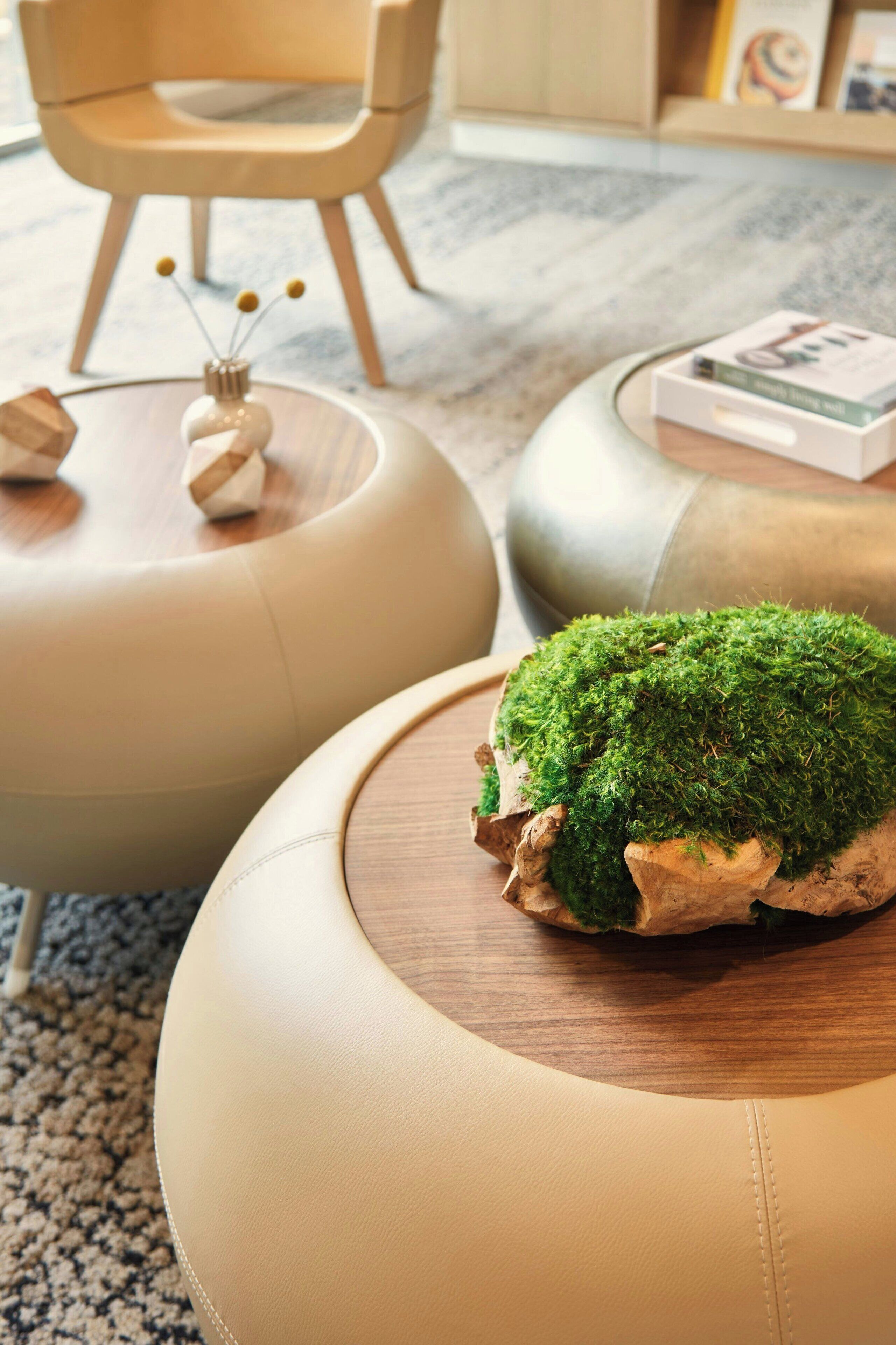 Una sala de estar moderna con un sofá redondo color beige, una mesa de centro de madera con cubierta que imita musgo, y un pequeño jarrón decorativo con diseño trenzado.