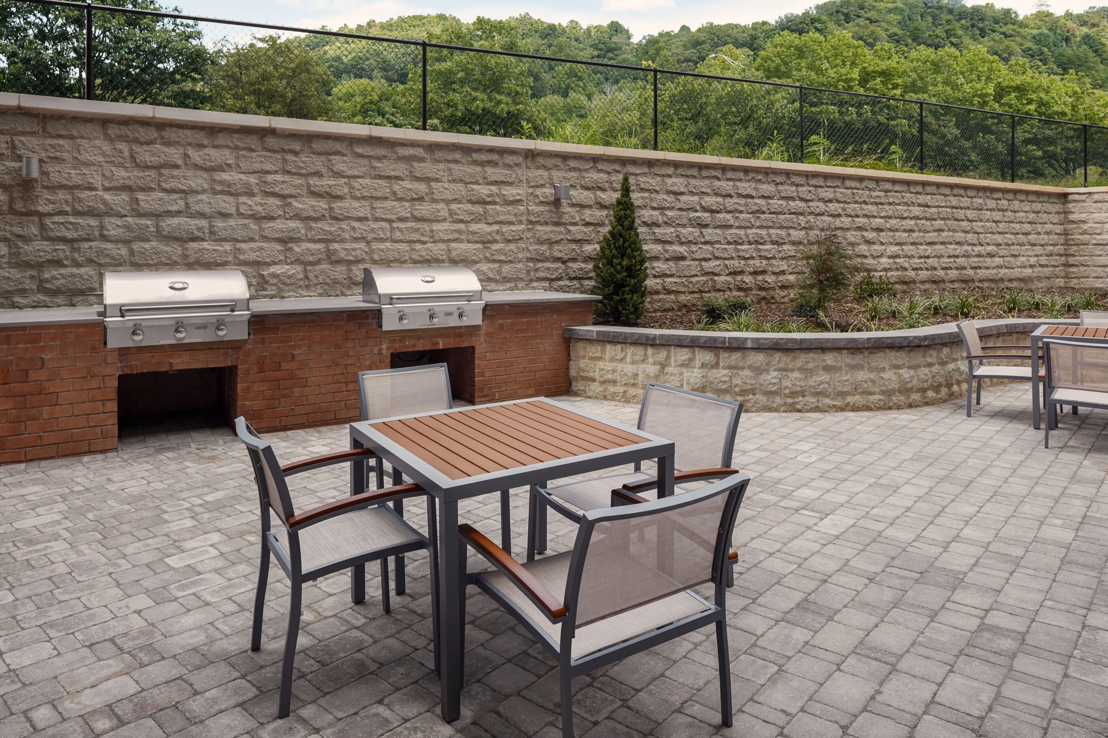 An outdoor patio with a brick barbecue area, a table, and chairs.