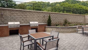 An outdoor patio with a brick barbecue area, a table, and chairs.