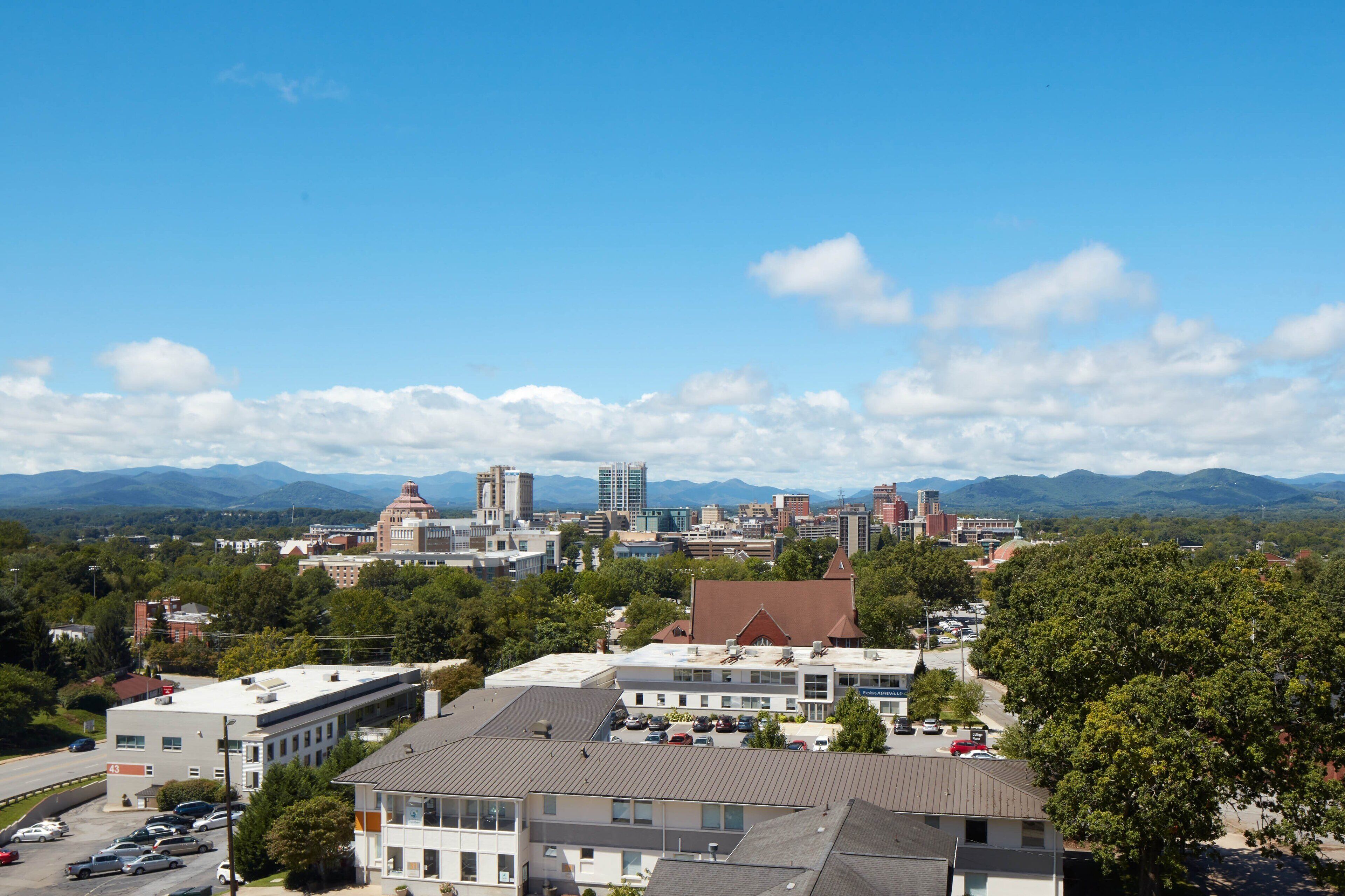 A cityscape with a mix of modern and historic buildings, a parking lot, and a view of distant mountains.