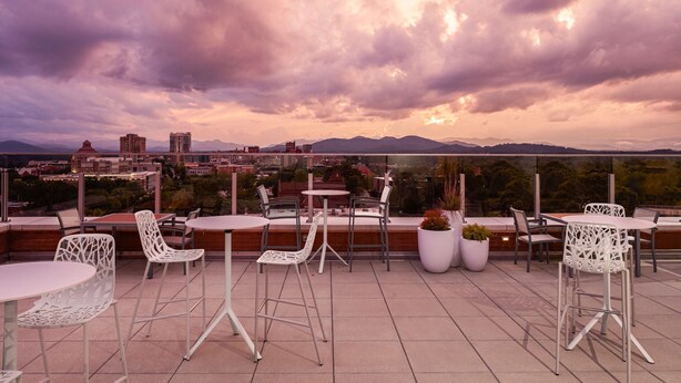 Eine Dachterrasse mit Sitzgelegenheiten im Freien, Topfpflanzen und Blick auf die Stadt.