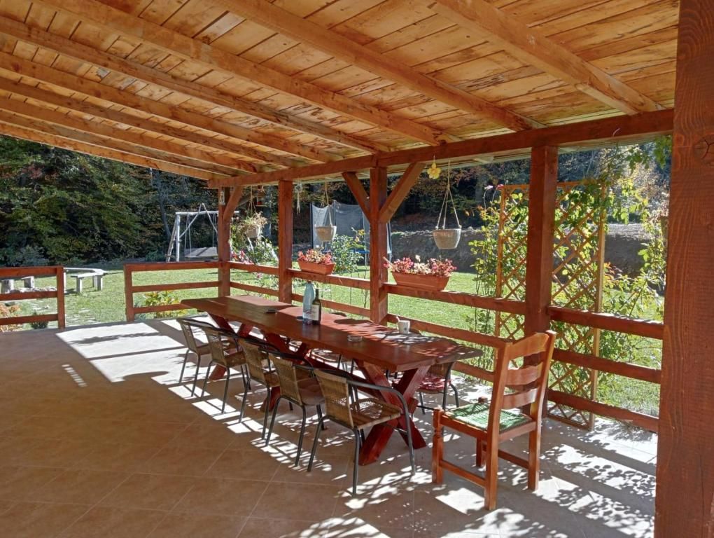 An outdoor wooden pergola with a table and chairs, surrounded by a garden with potted plants.