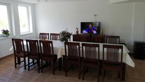 A dining area with a table set for six, wooden chairs, a television on a stand, and a ceiling fan. - Pensiunea Rozelor (Simbata de Sus)
