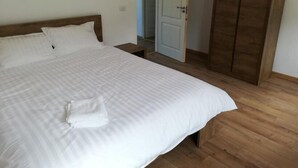A neatly made bed with white linens, a wooden headboard, and a wooden wardrobe in a room with wooden flooring. - Pensiunea Rozelor (Simbata de Sus)