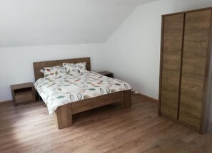 Ein Schlafzimmer mit einem Holzbett, einem Nachttisch, einem Kleiderschrank und einer schrägen Decke.