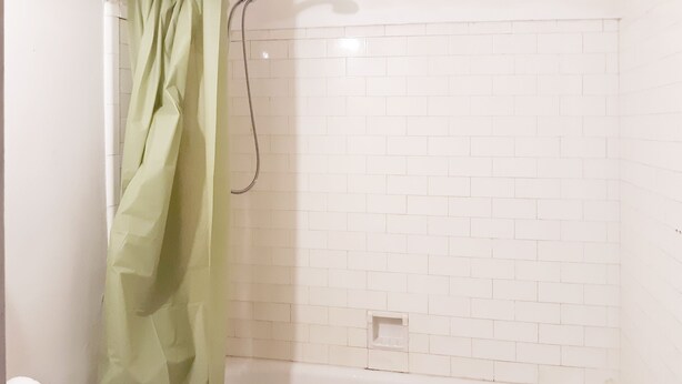 Ein Badezimmer mit Dusche, weißen Fliesenwänden und einem grünen Duschvorhang.