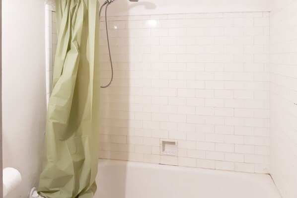 A bathroom with a shower, white tiled walls, and a green shower curtain. - Hotel Bradford Main St PA (Bradford)