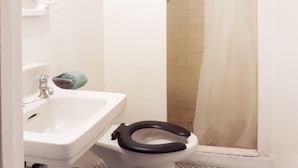 Ein Badezimmer mit einem weißen Waschbecken, einer Toilette mit schwarzem Sitz und einer Duschkabine mit Vorhang.