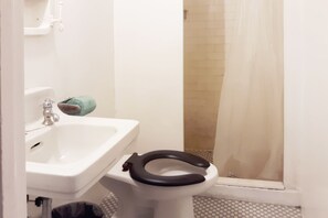 A bathroom with a white sink, a toilet with a black seat, and a shower area with a curtain. - Hotel Bradford Main St PA (Bradford)