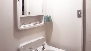 Ein Badezimmer mit Waschbecken, zwei Wasserhähnen, einem Spiegel und einem Toilettenpapierhalter.