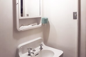 A bathroom with a white sink, two faucets, a mirror, and a toilet paper holder. - Hotel Bradford Main St PA (Bradford)